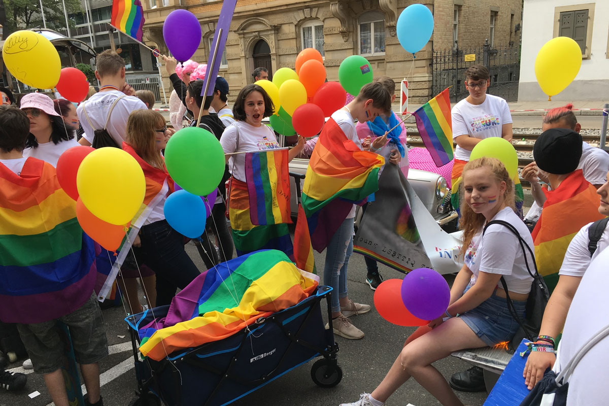 Gruppe junger Menschen mit Luftballons und Regenbogen-Fahnen